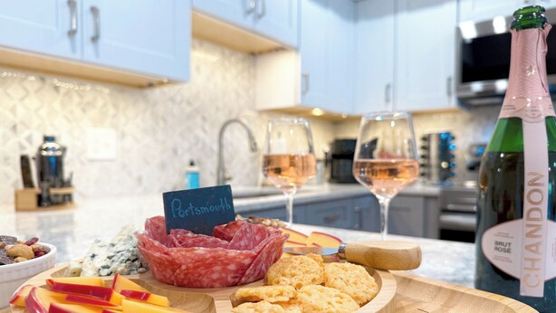 Une planche en bois garnie de différents fromages, de charcuteries et de fruits, le tout présenté dans une cuisine moderne.