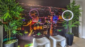 A room with a large cityscape mural, two white chairs, and two potted plants.