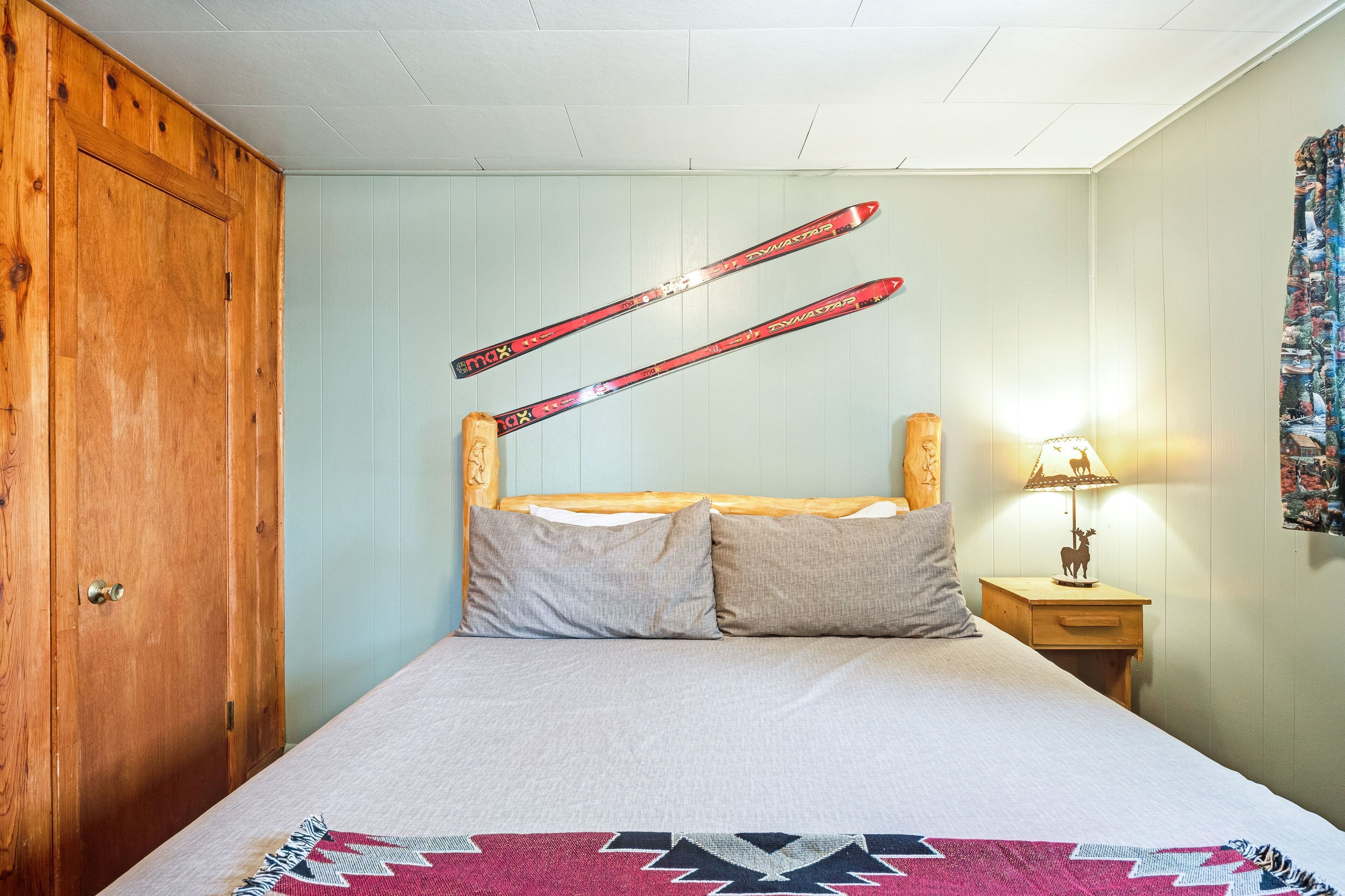 Un dormitorio con un armario de madera, una cama con una colcha estampada y esquíes colgados en la pared.