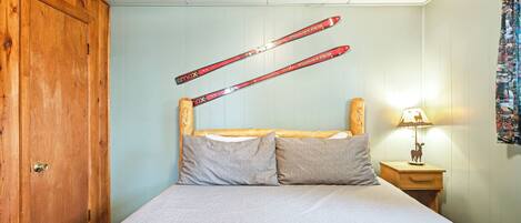 Un dormitorio con un armario de madera, una cama con una colcha estampada y esquíes colgados en la pared.