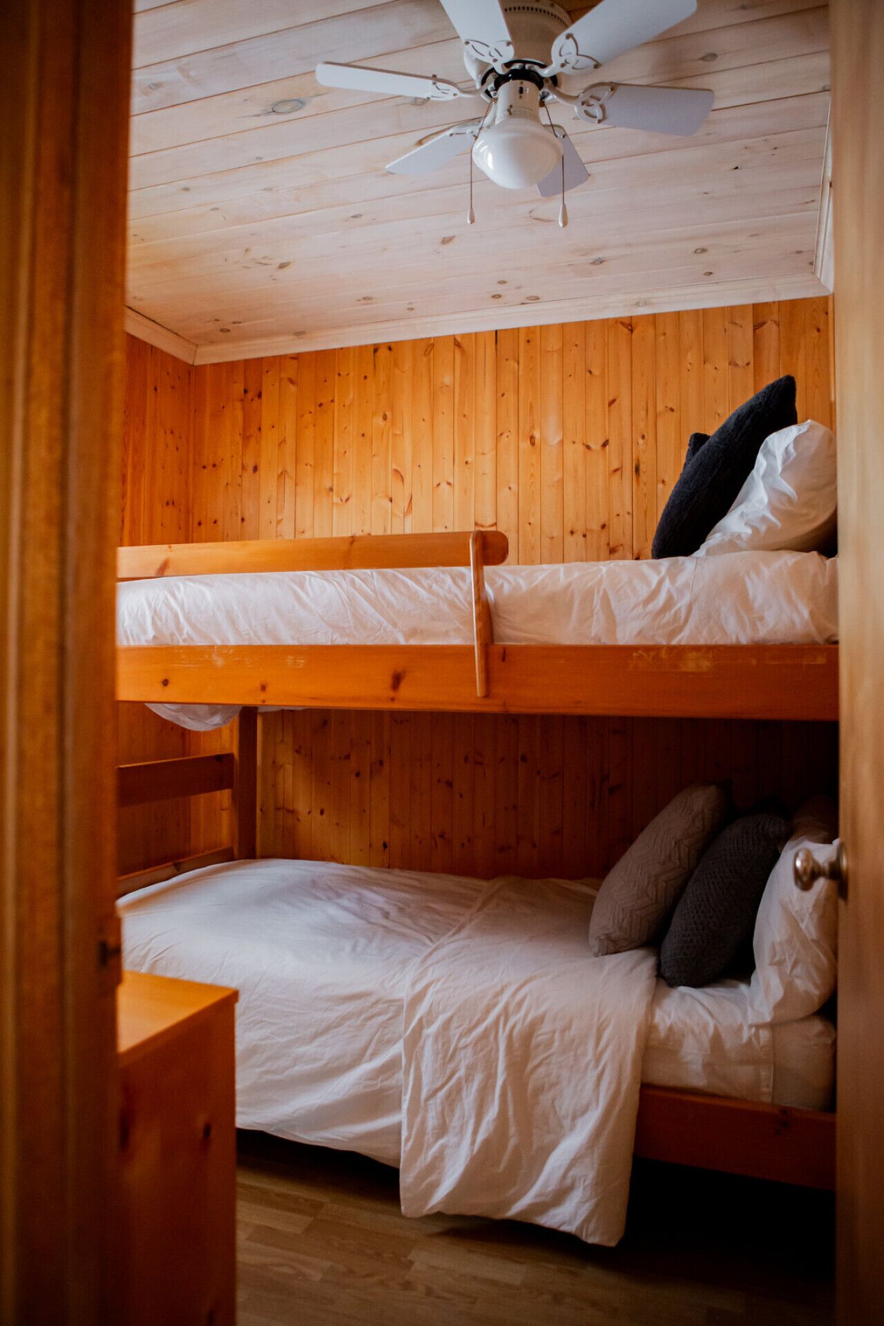 A bunk bed room with wooden walls and a ceiling fan.