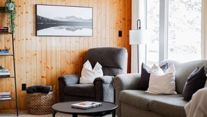Un salon chaleureux avec un mur en bois, un fauteuil gris, un canapé gris et une table basse ronde.