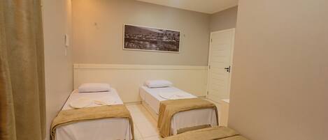 Een hotelkamer met twee enkele bedden, een witte deur en een ingelijst schilderij aan de muur.