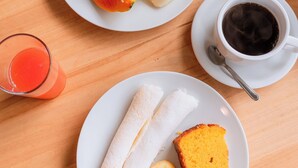 Una escena de desayuno con un plato de fruta, un vaso de jugo, una taza de café y un plato con pan y huevos.