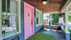 A porch with a swing set, a pink door, and a blue and green house.