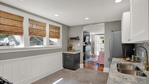 A modern kitchen with a central island, white cabinetry, and a large window with bamboo blinds.