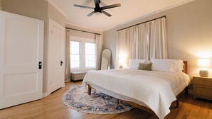 A bedroom with a bed, a ceiling fan, a bedside table with a lamp, and a round rug. - Luxe Cottage, Near Downtown and Ocean, Backyard Fire Pit, King Bed (Corpus Christi)