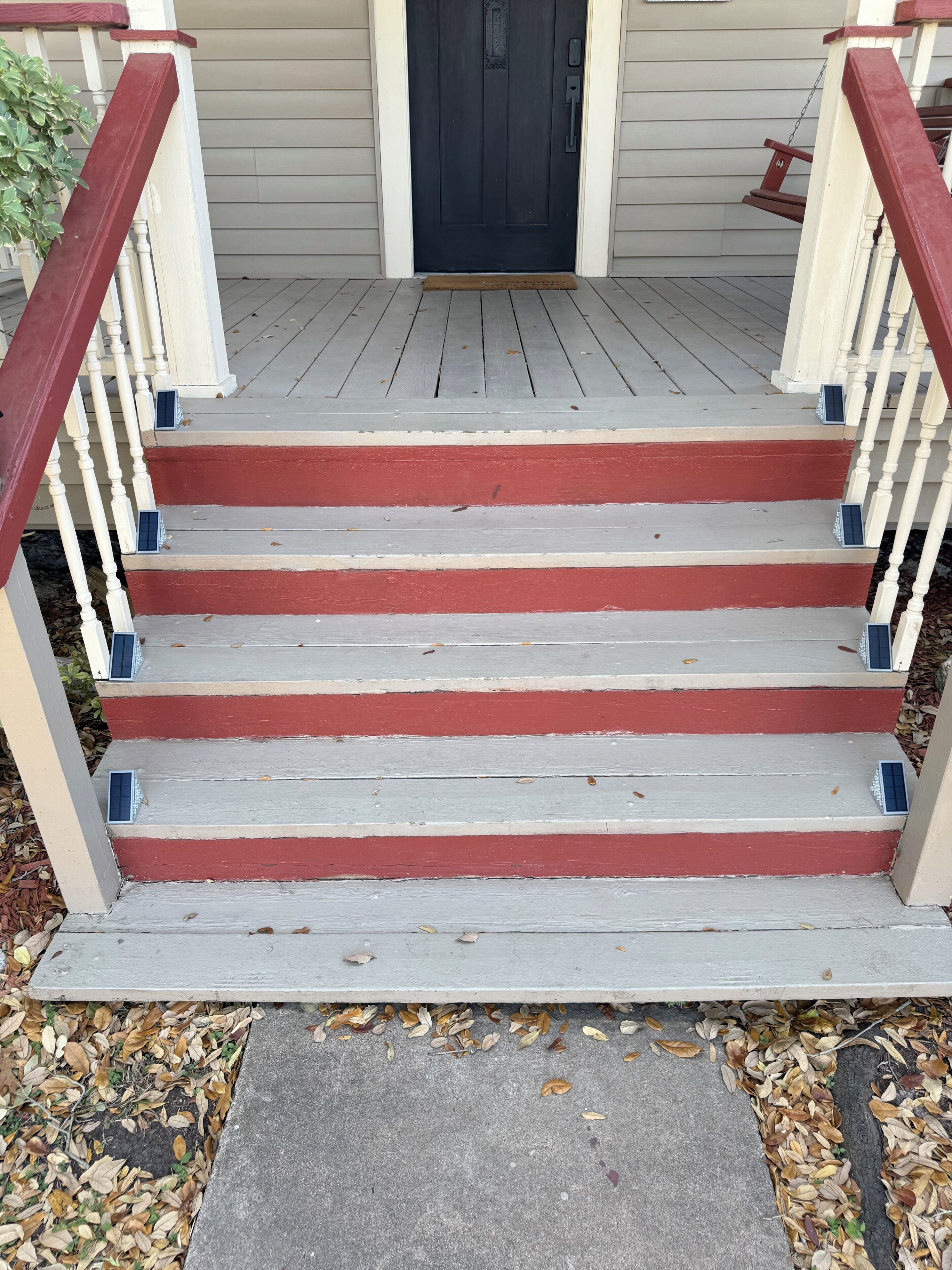 A wooden staircase with red and white steps leading to a dark door.