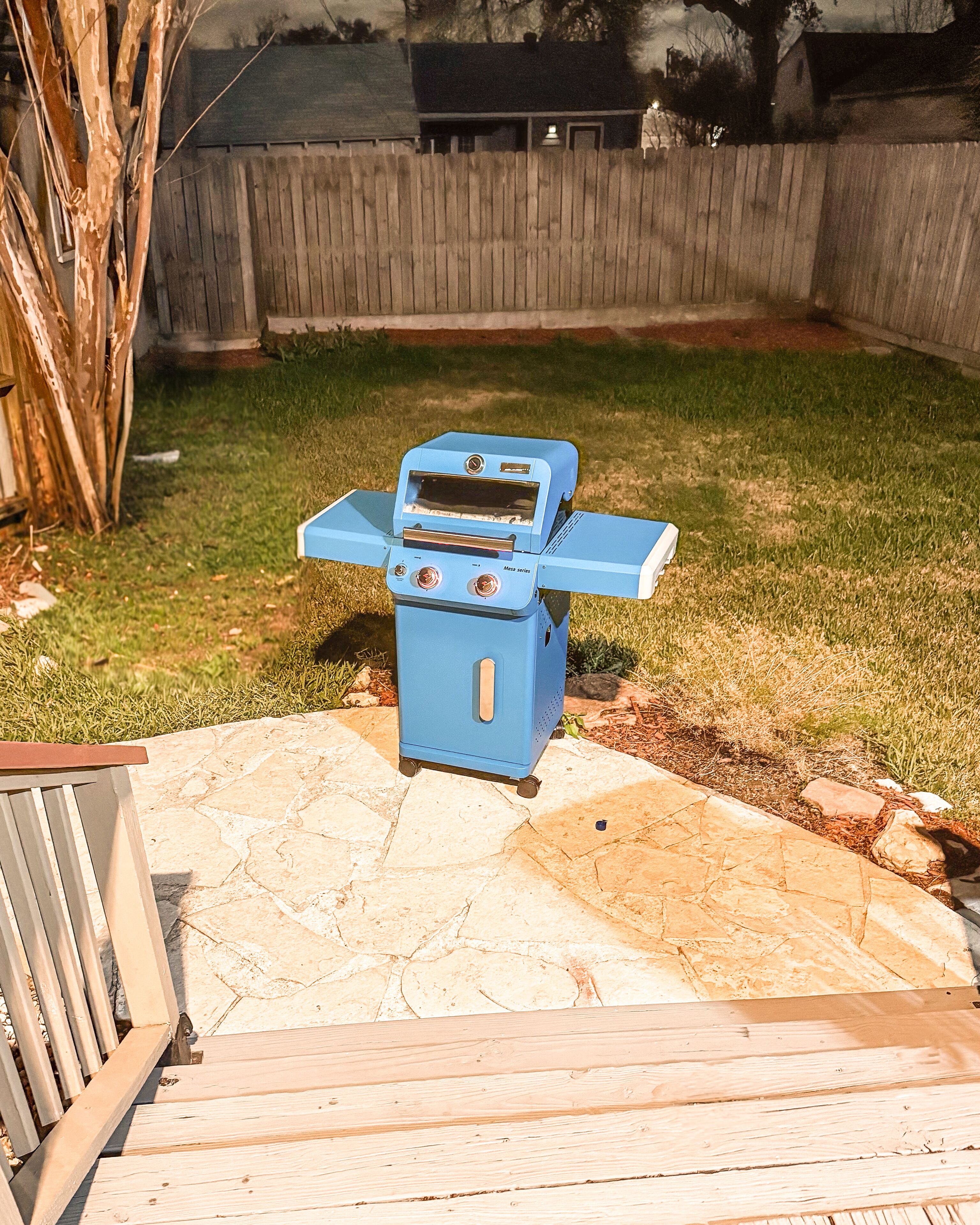A blue outdoor grill with a control panel, situated on a patio with a stone floor.