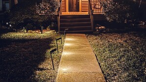 A well-lit wooden house with a concrete pathway leading to the front door. - Luxe Cottage, Near Downtown and Ocean, Backyard Fire Pit, King Bed (Corpus Christi)