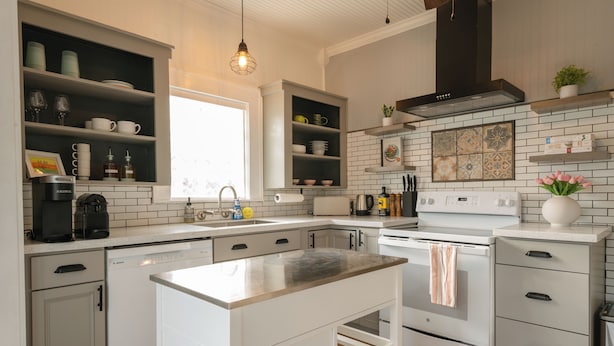 A modern kitchen with white cabinetry, a central island, a built-in dishwasher, and a stainless steel range hood. - Luxe Cottage, Near Downtown and Ocean, Backyard Fire Pit, King Bed (Corpus Christi)