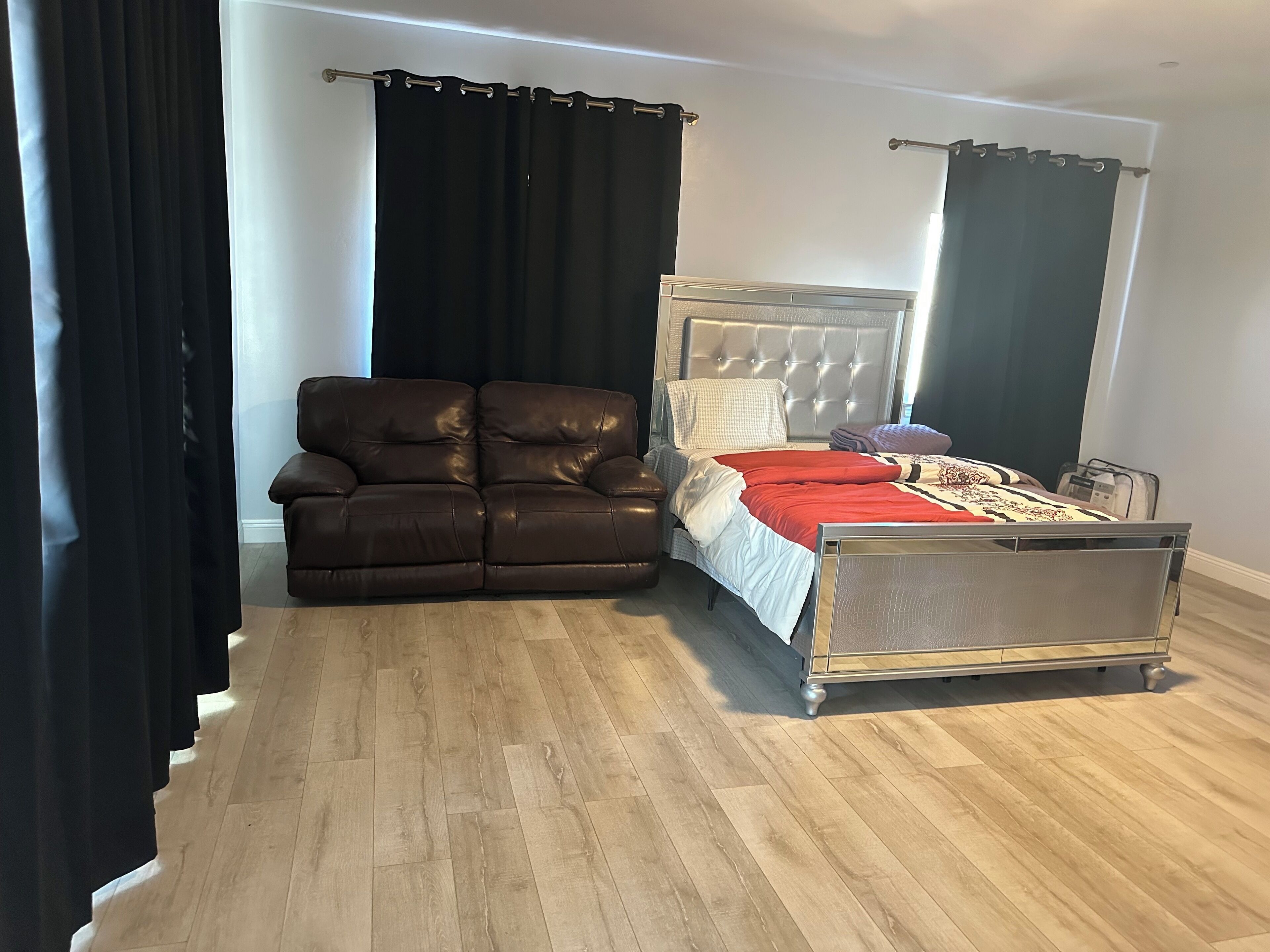 Quarto com cama, sofá e piso de madeira.