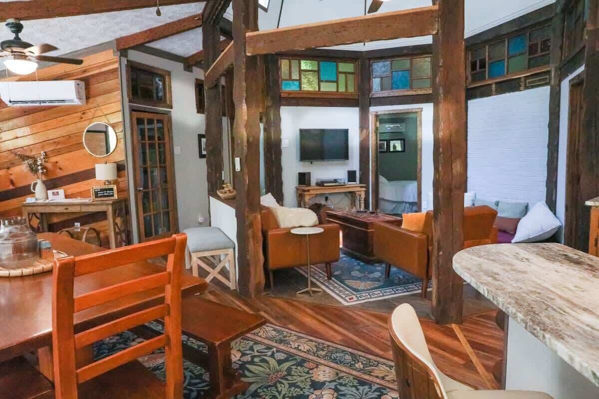 Un intérieur chaleureux avec des poutres en bois, un coin repas, un espace détente avec des coussins et un téléviseur.