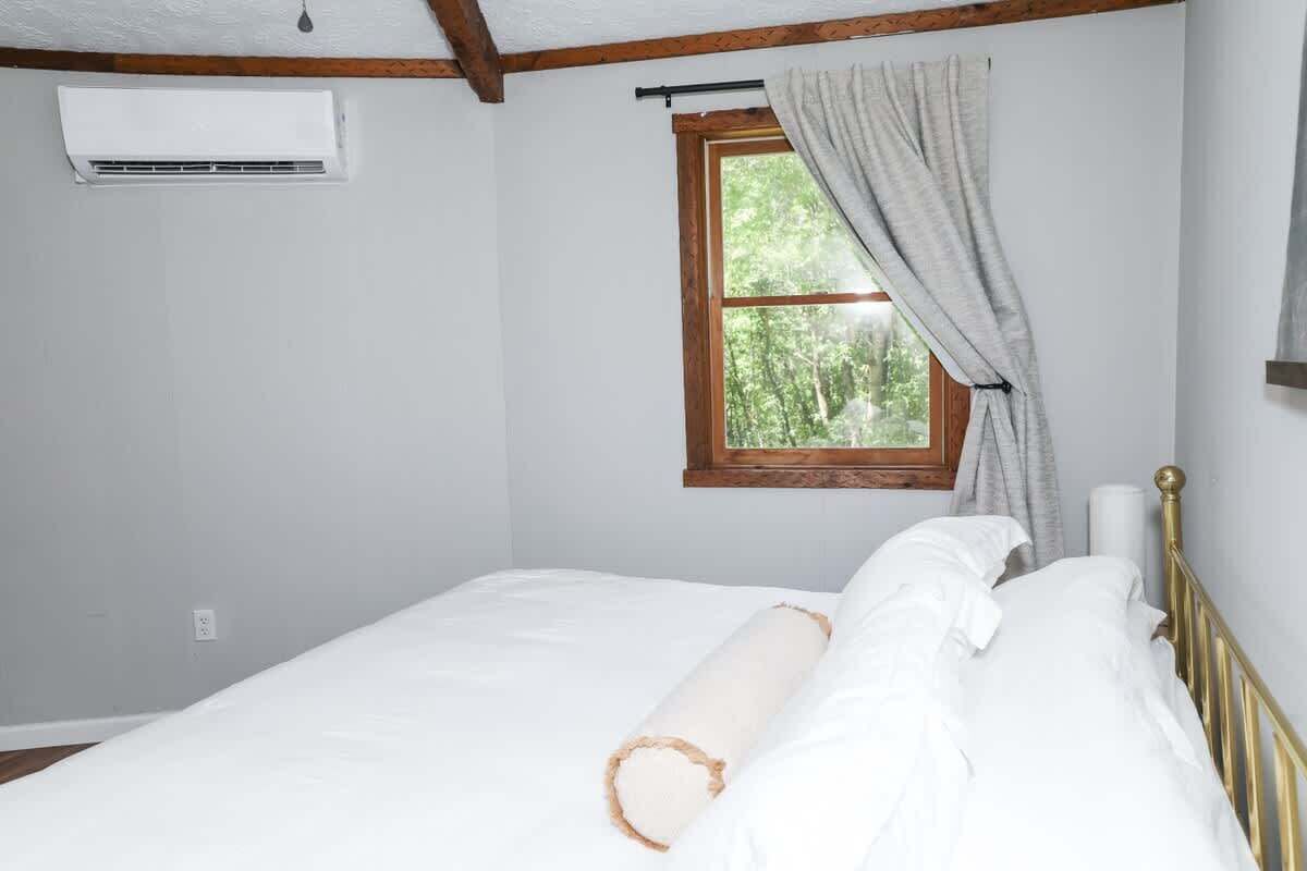 Ein Schlafzimmer mit einem Einzelbett, einem Fenster mit Vorhängen, einer Klimaanlage und einem Holzbalken an der Decke.