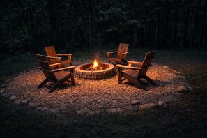 Un focolare in pietra circolare con un fuoco acceso al centro, circondato da quattro poltrone in legno di tipo Adirondack.