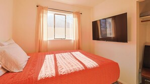 A bedroom with a bed, a window with curtains, a flat-screen TV mounted on the wall, and a closet with a mirror.