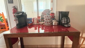 A kitchen counter with a coffee maker, a kettle, a mug, and a tray of food items.