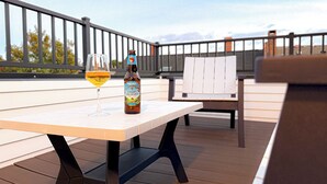 A table with a bottle of Angry Orchard cider and a glass of cider on an outdoor deck.