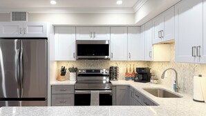 A modern kitchen with stainless steel appliances, white cabinetry, and a granite countertop.