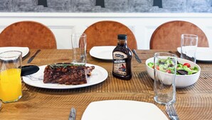 A dining table with plates, a bottle of sauce, and glasses of water.