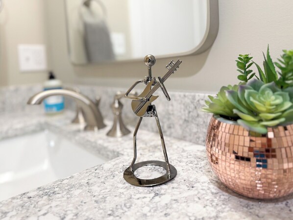 Un lavamanos de baño con una figurita metálica, una suculenta en maceta y un espejo.