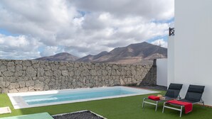 A pool with two lounge chairs, a stone wall, and a mountain view. - Vacation Villa 'Luxury  Lanzarote' with Sea View, Private Pool and Wi-Fi (Playa Blanca)