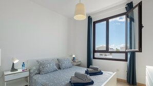 A bedroom with a bed, bedside tables, a lamp, a window with curtains, and a view of buildings outside. - Vacation Villa 'Luxury  Lanzarote' with Sea View, Private Pool and Wi-Fi (Playa Blanca)