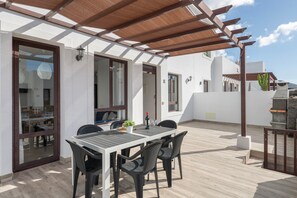 A covered patio with a table and chairs, a pergola, and a view of the interior.