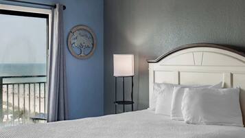Et hotelværelse med en seng, et natbord med en lampe, et vægur og udsigt til stranden.