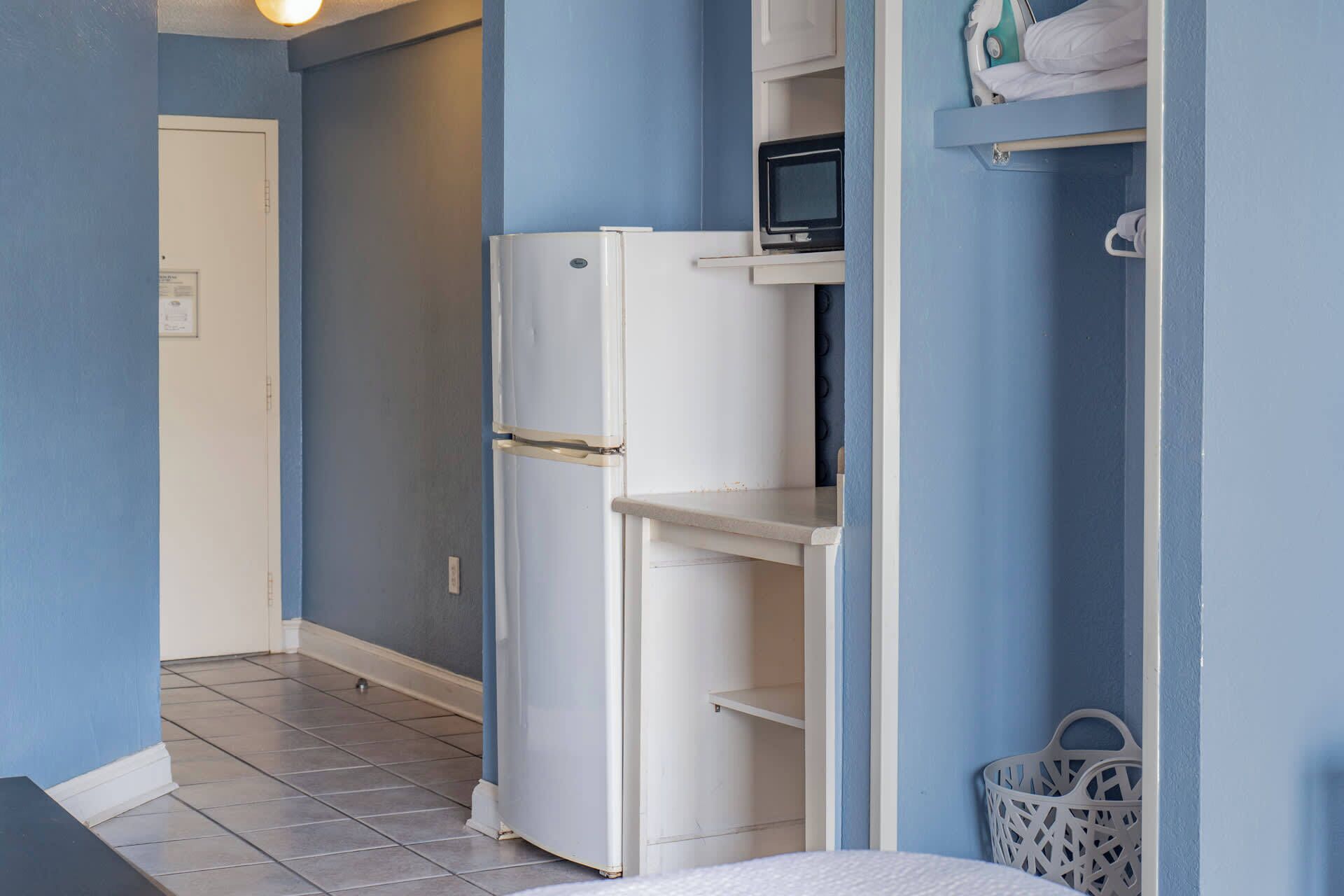 A compact kitchenette with a white refrigerator, a microwave, and a small shelf.
