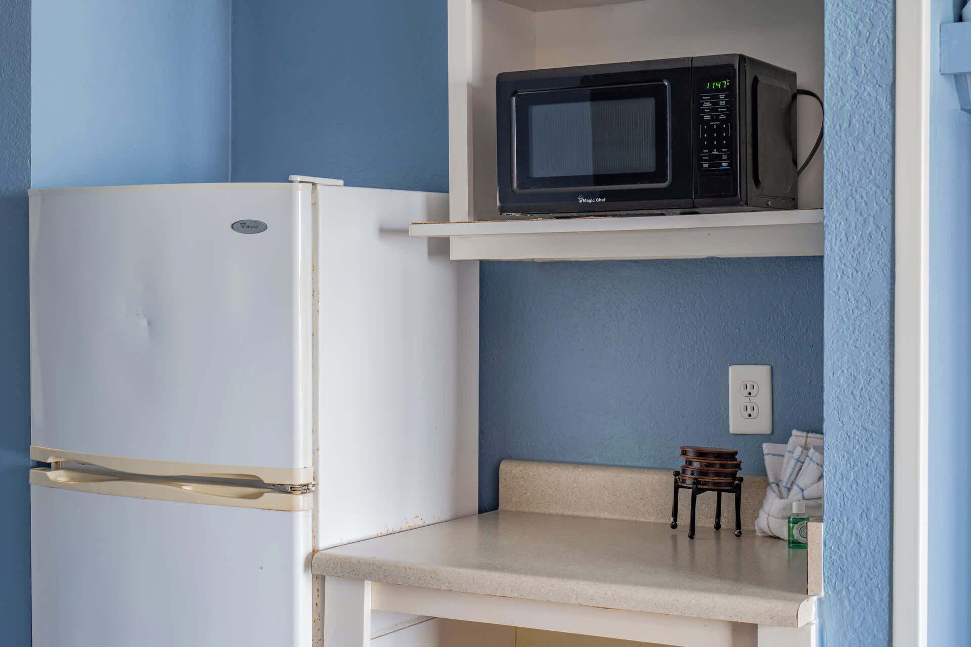 A kitchen with a white refrigerator, a microwave on a shelf, and a small wooden stool.