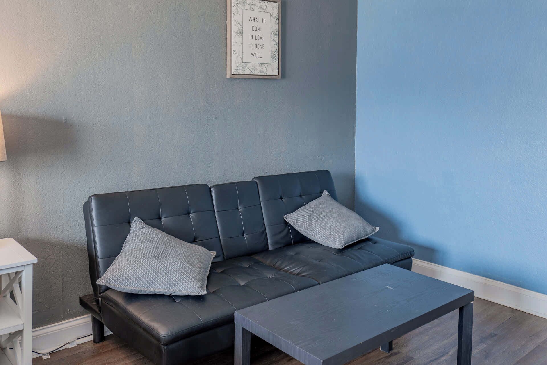 A modern living room with a dark leather sofa, two matching cushions, and a small table.