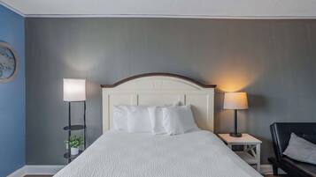 Et hotelværelse med en seng, sengeborde, lamper, en stol og en lampe på væggen.