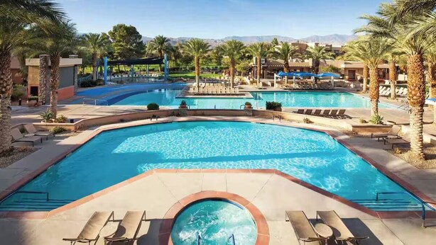 Ein Poolbereich eines Resorts mit mehreren Schwimmbecken, Liegestühlen und Palmen.