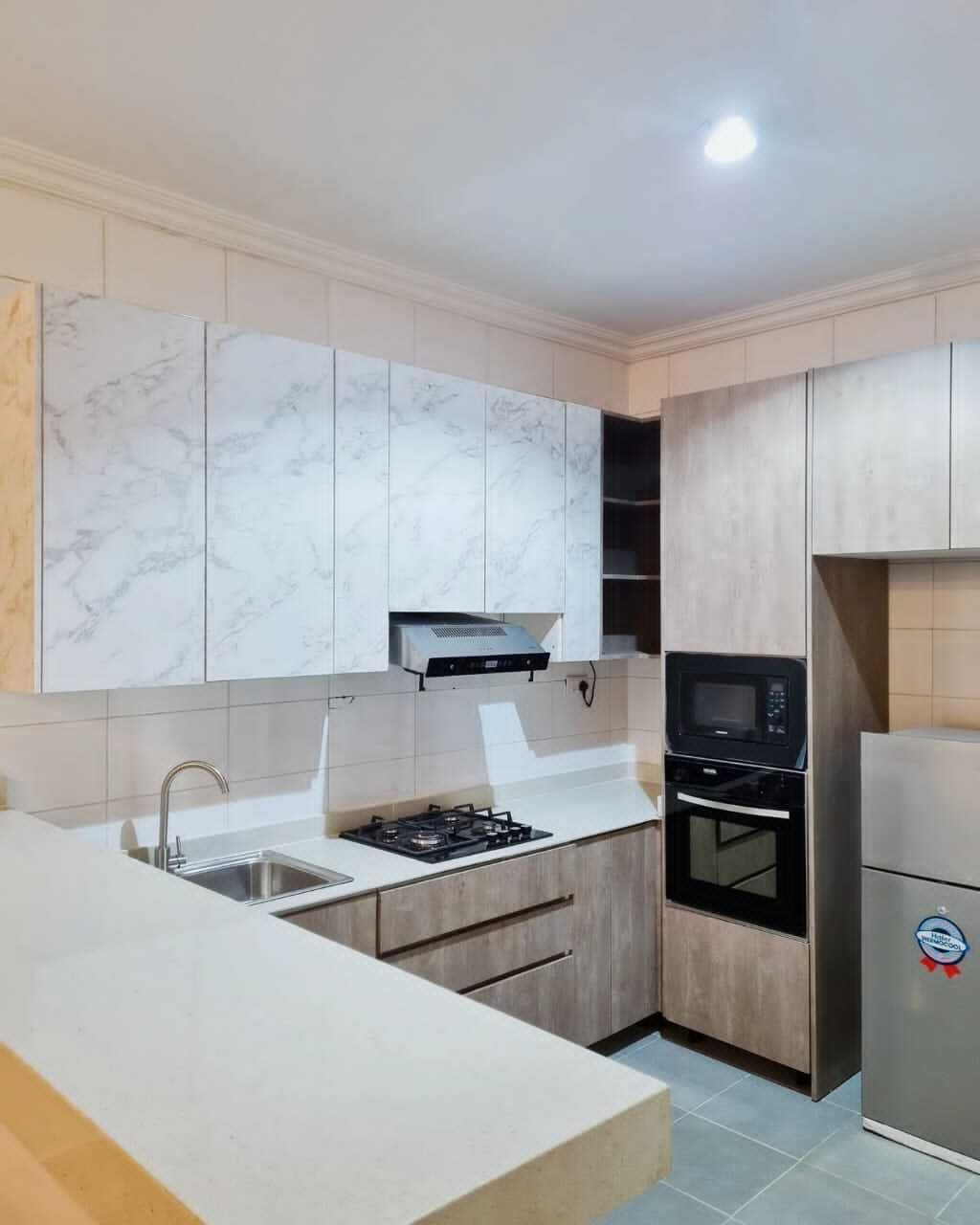 A modern kitchen with marble cabinets, a stainless steel refrigerator, a microwave, and a gas stove.
