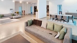 A modern living room with a sofa, coffee table, and dining area with chairs. - Boya Apartments (Abuja)