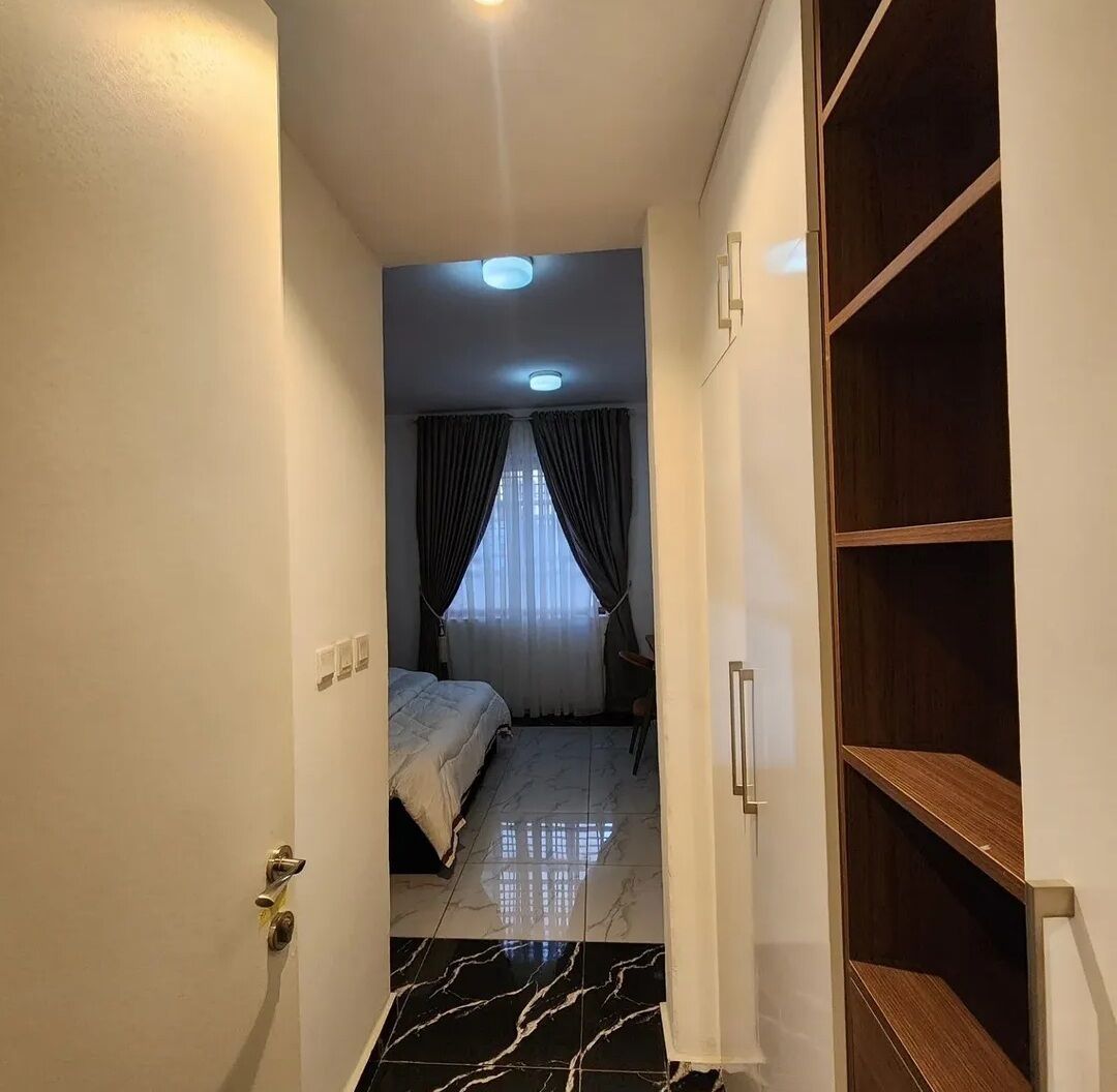 A hotel room with a bed, a wooden wardrobe, a bathroom with a mirror, and a tiled floor.