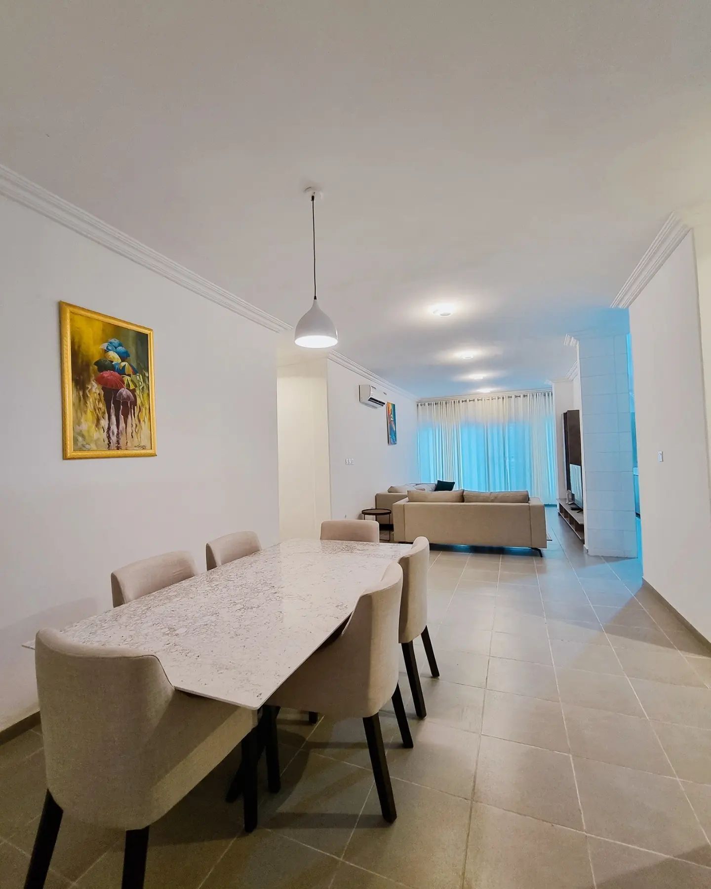 Uma sala de estar ampla com uma mesa de jantar, sofás e um quadro na parede.