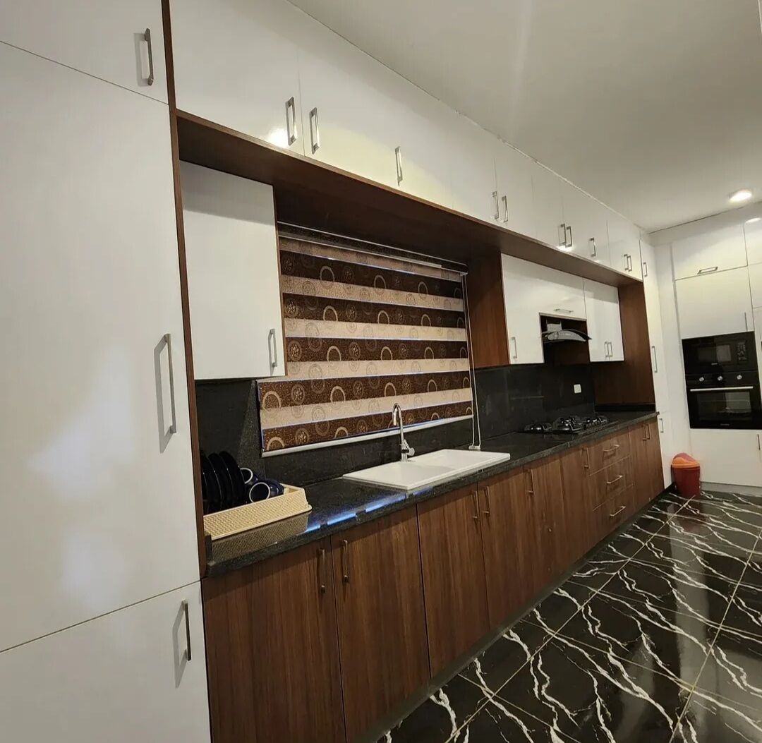 A modern kitchen with white cabinets, a patterned backsplash, a black countertop, and a marble floor.