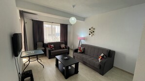 A living room with a sofa, armchair, coffee table, TV, and a lamp. - Elma Hotel (Bar)