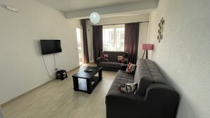 A living room with a sofa, a coffee table, a TV, and a lamp. - Elma Hotel (Bar)