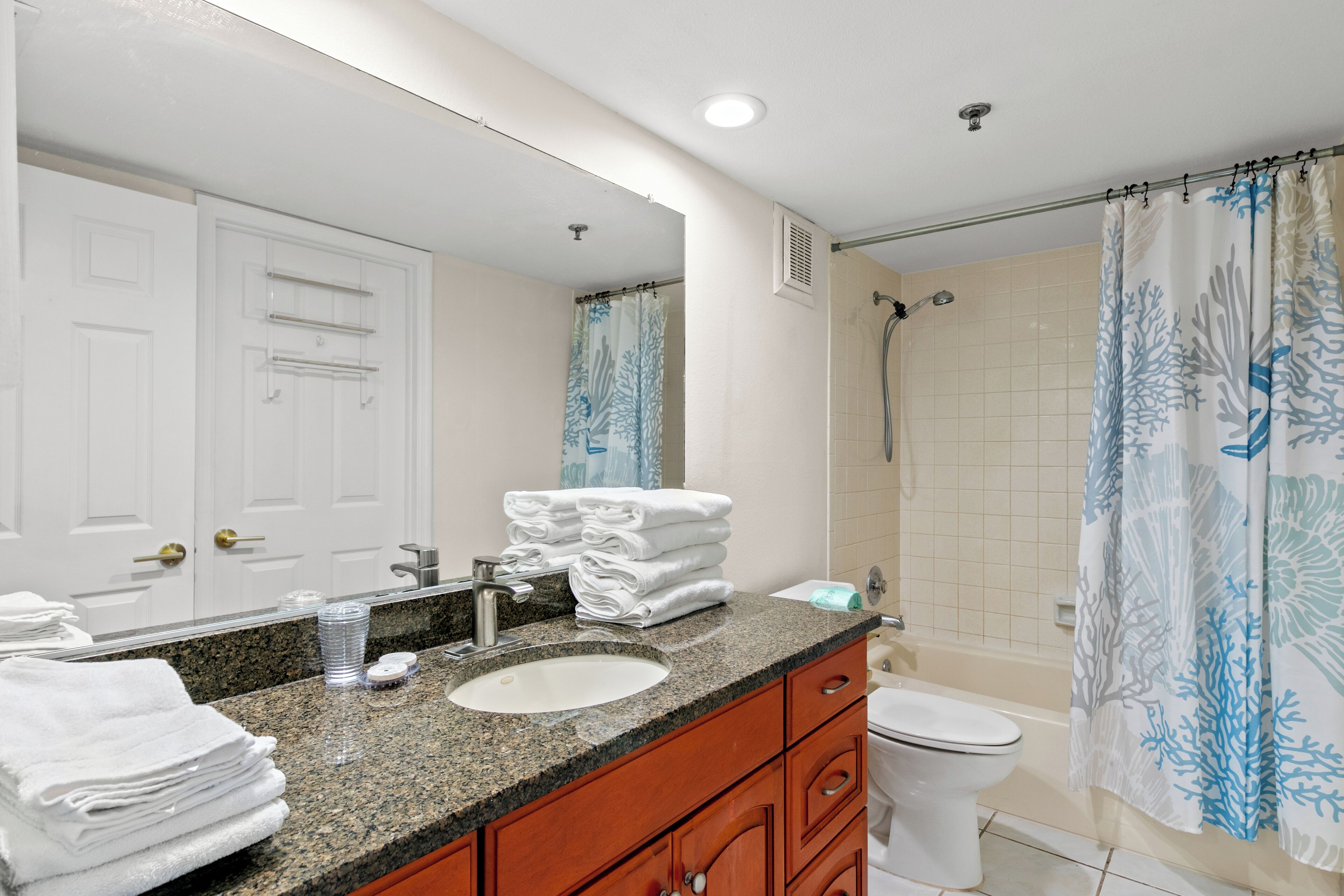 A bathroom with a sink, mirror, towel stack, toilet, and shower curtain.