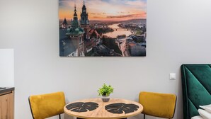 A dining area with a round wooden table, two mustard-colored chairs, and a cityscape painting on the wall. - Underground Basilica Apartment (Kraków)