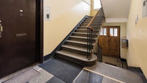 A staircase with a wooden handrail and a black metal railing, leading to a wooden door with a window. - Underground Basilica Apartment (Kraków)