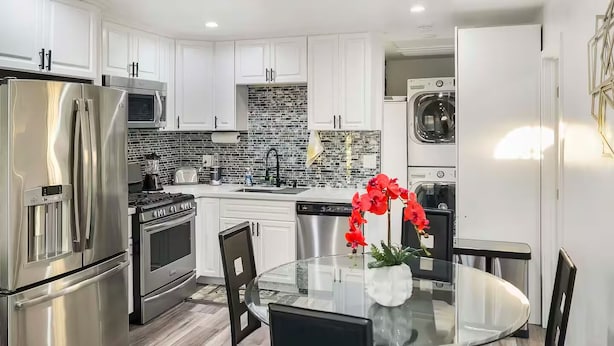 A modern kitchen with white cabinets, stainless steel appliances, a tiled backsplash, and a glass dining table with chairs. - The Shalimar Casita, Fits 6 Guests, Smart Tvs, Remodeled Unit, Full Size Kitchen (Riverside)
