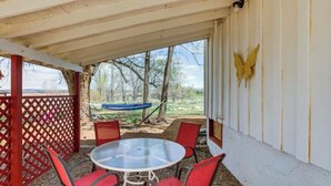 Un patio techado con una mesa redonda de vidrio y sillas rojas, una hamaca y una decoración de mariposa en la pared.