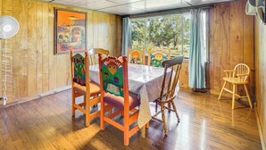 Un comedor con una mesa y sillas de madera, un ventilador y una ventana con cortinas.