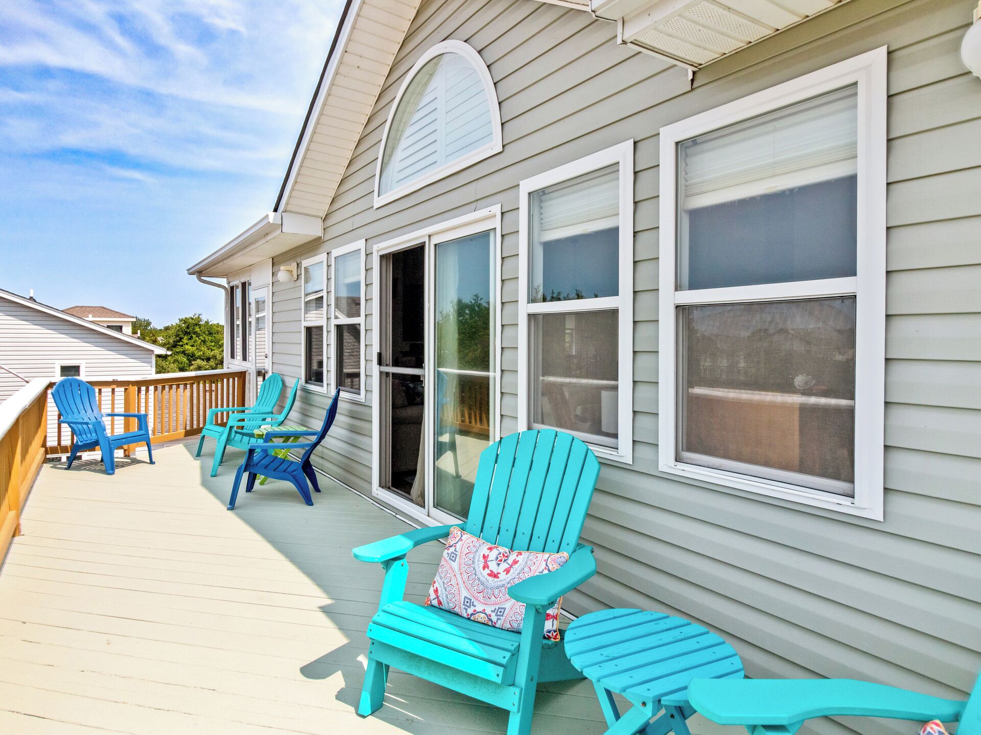 A covered deck with turquoise Adirondack chairs and a wooden railing.