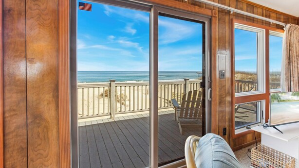 A wooden deck with a view of the ocean, a chair, and a table with a basket. - 7050 Sailor's Rest at Nags Head * Oceanfront (Nags Head)