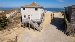 A two-story beach house with a wooden deck and stairs leading to a beach area. - 7050 Sailor's Rest at Nags Head * Oceanfront (Nags Head)